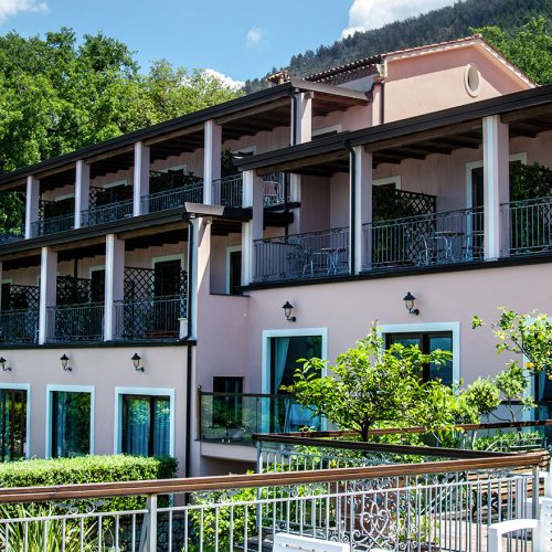 Un elegante edificio rosa con balconi affacciati su un giardino verde e rigoglioso.